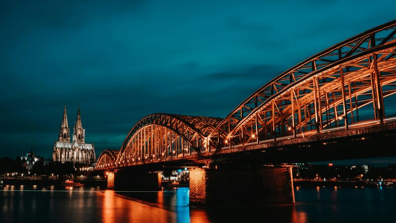 Illuminated Hohenzollern Bridge in Cologne at night, with Cologne Cathedral rising in the background.