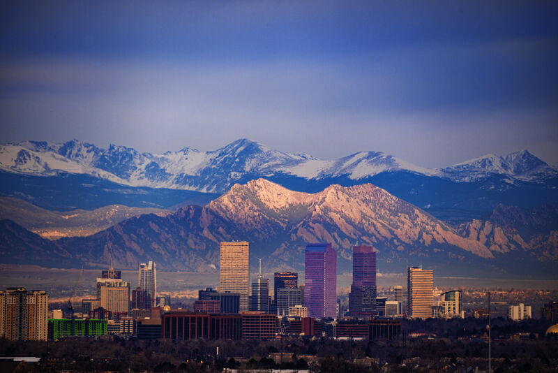 Denver skyline set against the Rocky Mountains, with snow‑capped peaks rising behind the city.