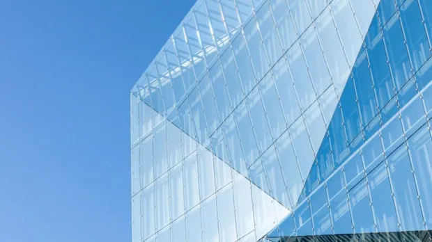 Modern glass building with angular design against a clear blue sky.