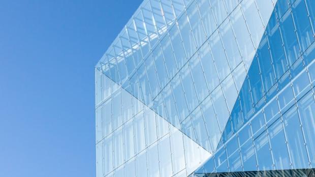 Modern glass building with angular design against a clear blue sky.