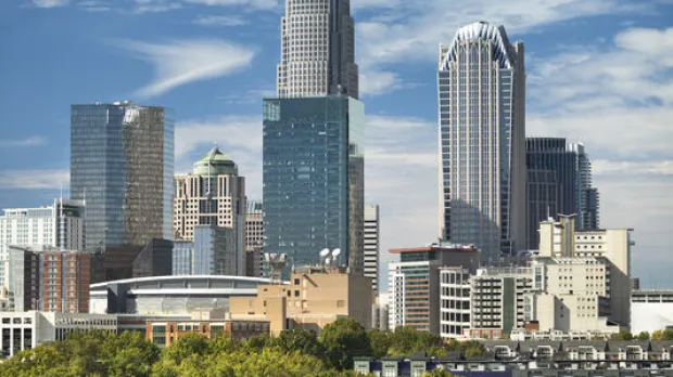 Charlotte skyline rising above green trees and residential buildings on a clear day.